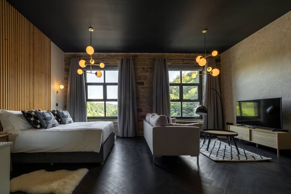 Ein modernes Schlafzimmer mit Bett, Sofa, Fernseher und großen Fenstern.
