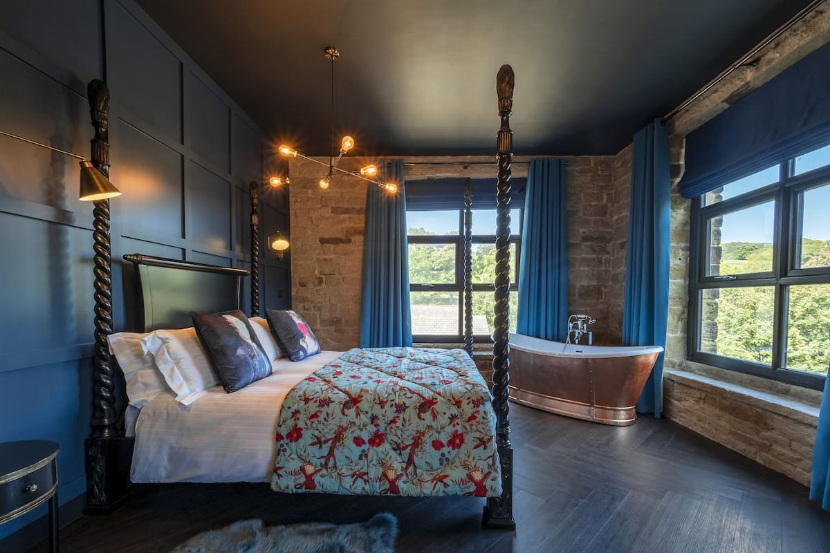 Ein Bett mit Baldachin, eine Badewanne mit Füßen und Blick auf Grün hinter großen Fenstern.