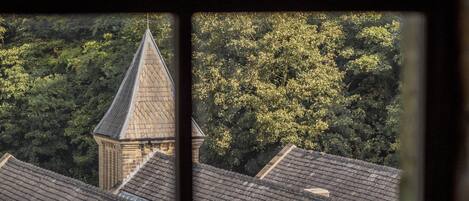 A view through a window of a building with a pointed roof and a brick structure, surrounded by dense green foliage.