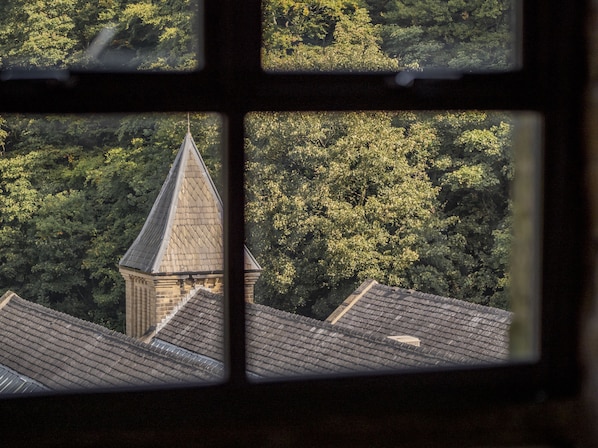 A view through a window of a building with a pointed roof and a brick structure, surrounded by dense green foliage.