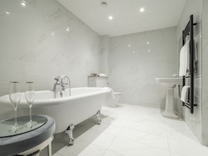 A modern bathroom with a freestanding bathtub, a glass-topped vanity, and a pedestal sink.