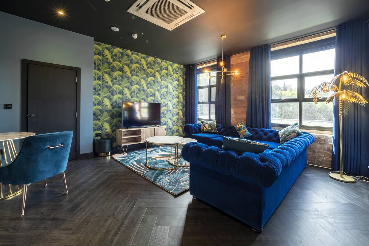 Ein modernes Wohnzimmer mit einem blauen Sofa, einem Flachbildfernseher und einem gemusterten Teppich.