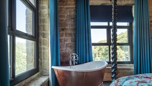 A bathroom with a freestanding copper bathtub, large windows with blue curtains, and a view of greenery outside. - Bowers Mill Aparthotel (Halifax)