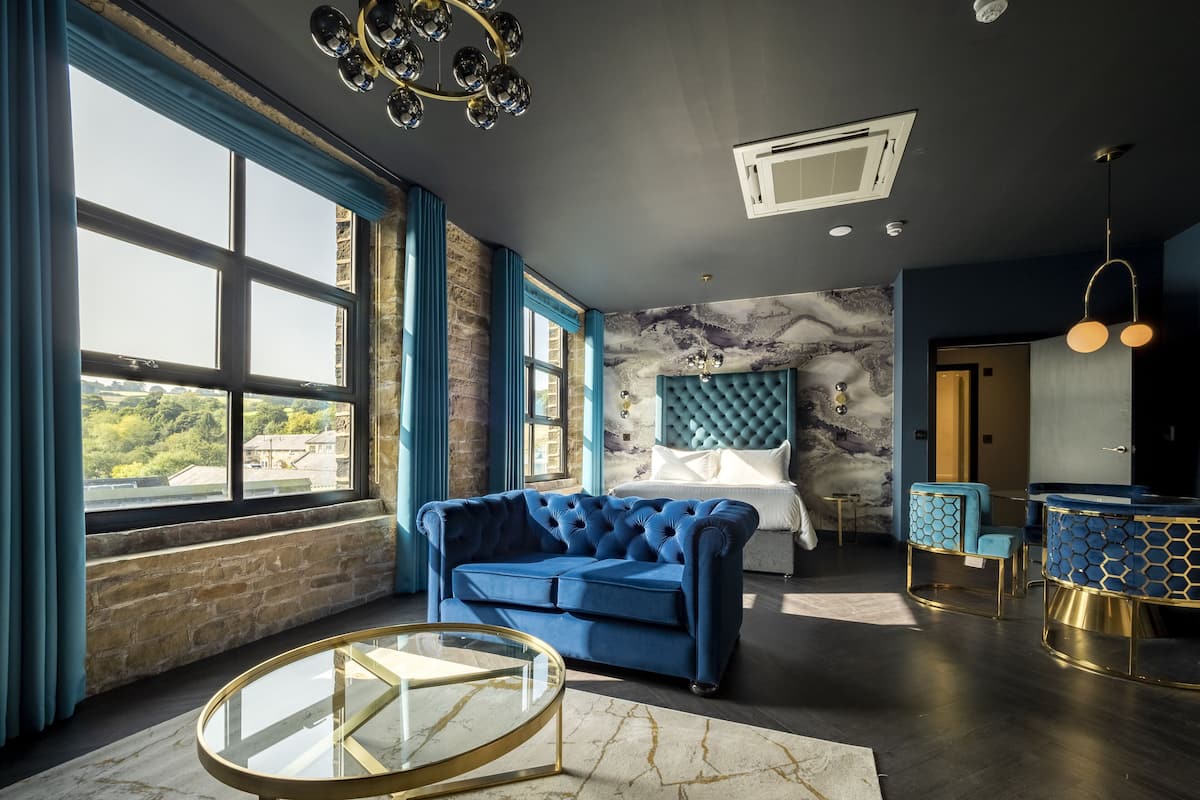 Ein modernes Schlafzimmer mit großem Fenster, einem gesteppten Kopfteil, einem runden Glastisch und einem Teppich mit Marmoroptik.