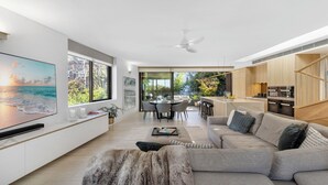Ein modernes Wohnzimmer mit großem Flachbildfernseher, einer Couch, einem Couchtisch und einem Essbereich mit Stühlen.