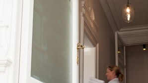 Eine Person trägt einen Stapel weiße Handtücher und steht in einer Diele mit einer weißen Tür und einer Pendelleuchte.