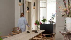 Ein Essbereich mit Holztisch und Stühlen, einer Vase mit Blumen und Pendelleuchten.