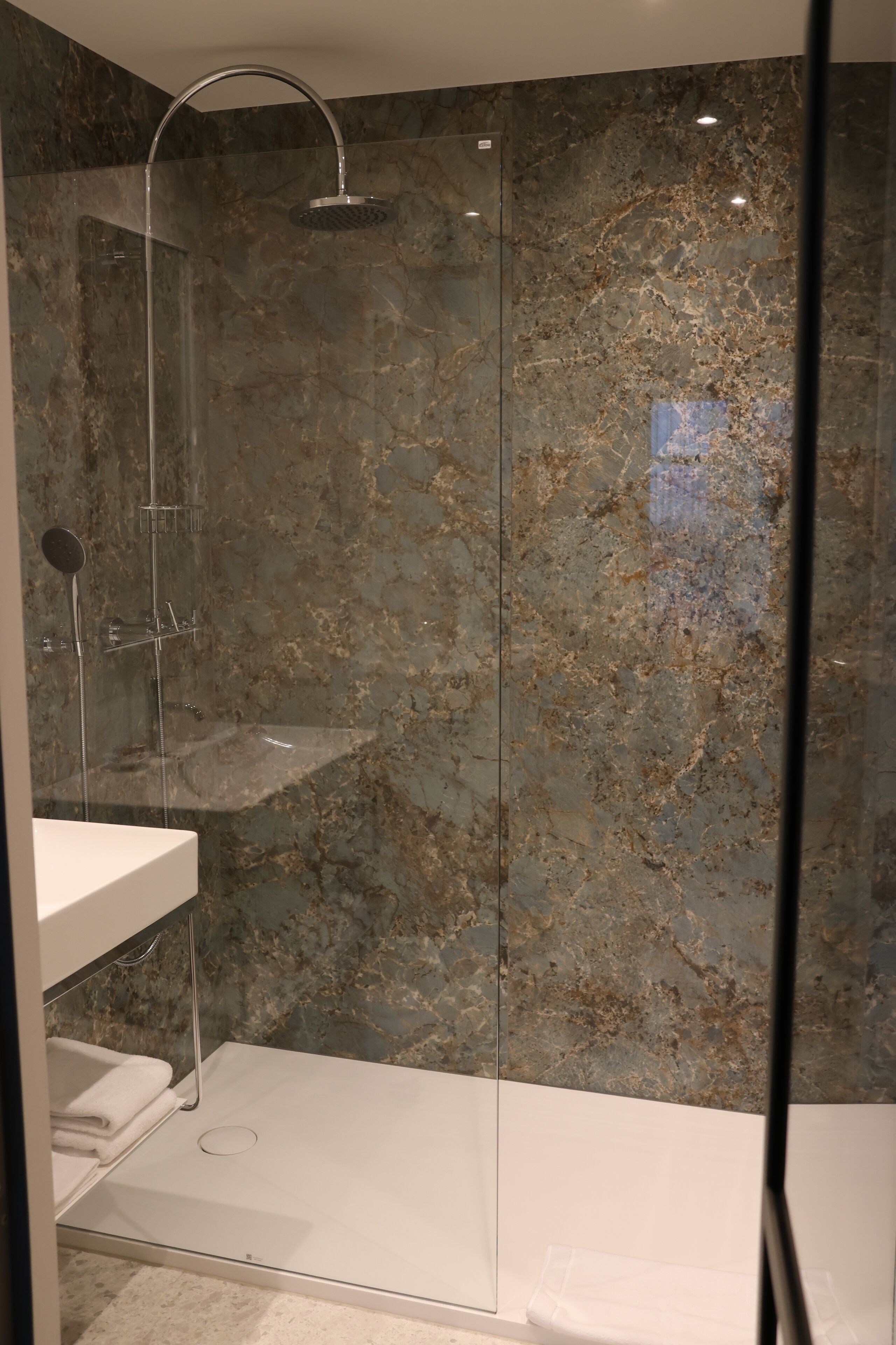 Un baño moderno con ducha de vidrio, paredes de mármol y lavamanos blanco.