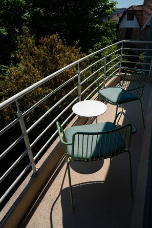 A balcony with a metal railing, two green chairs, and a small round table. - Hotel Iris (De Panne)