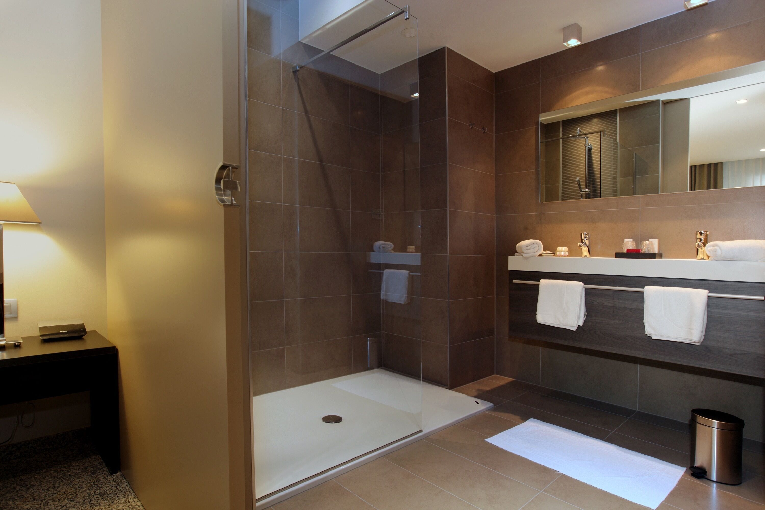 Een moderne badkamer met een douchecabine van glas, een wastafel met spiegel en een prullenbak.