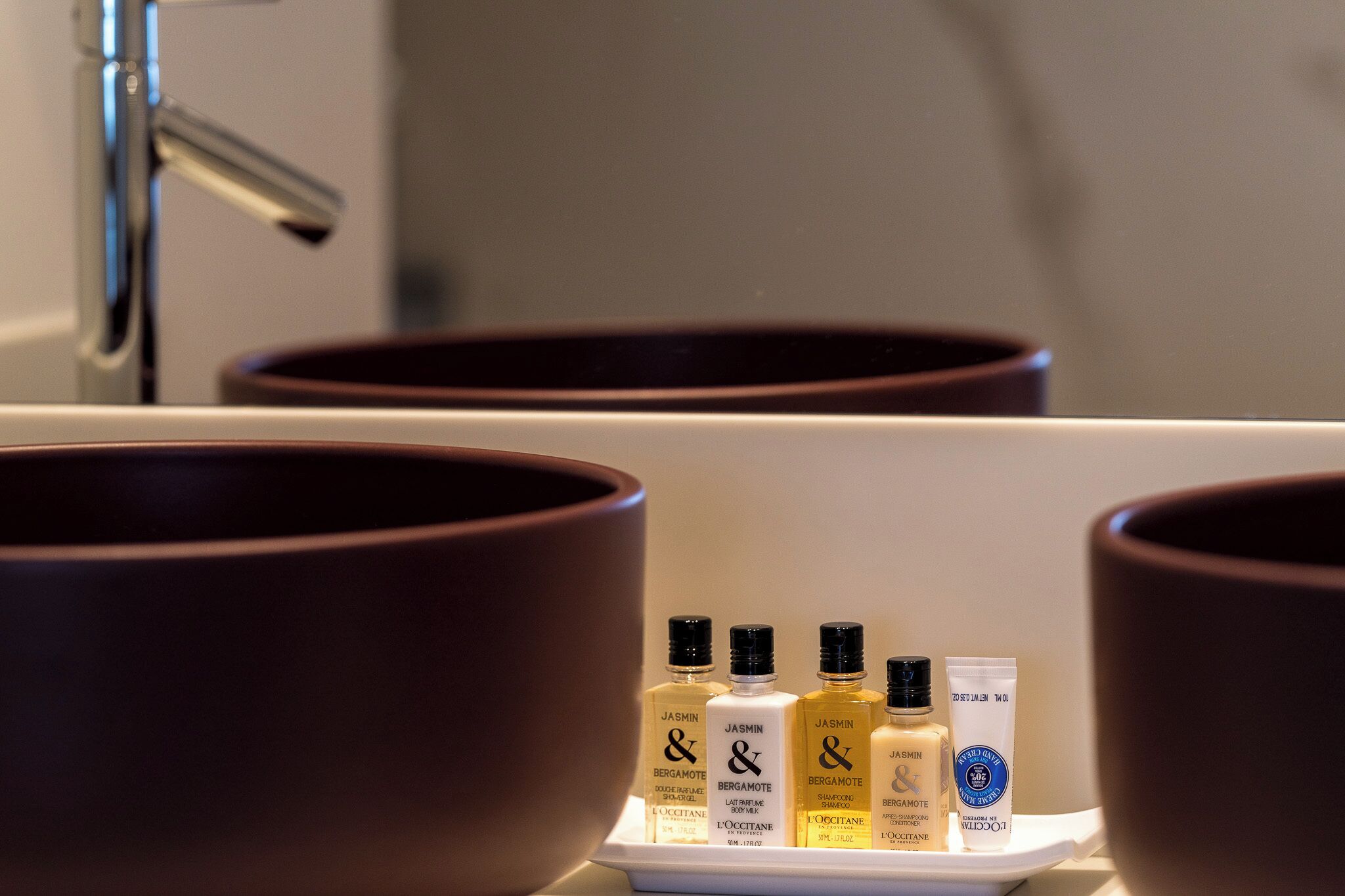 A bathroom with large brown basins and a tray holding several toiletries including shampoos and a cream.