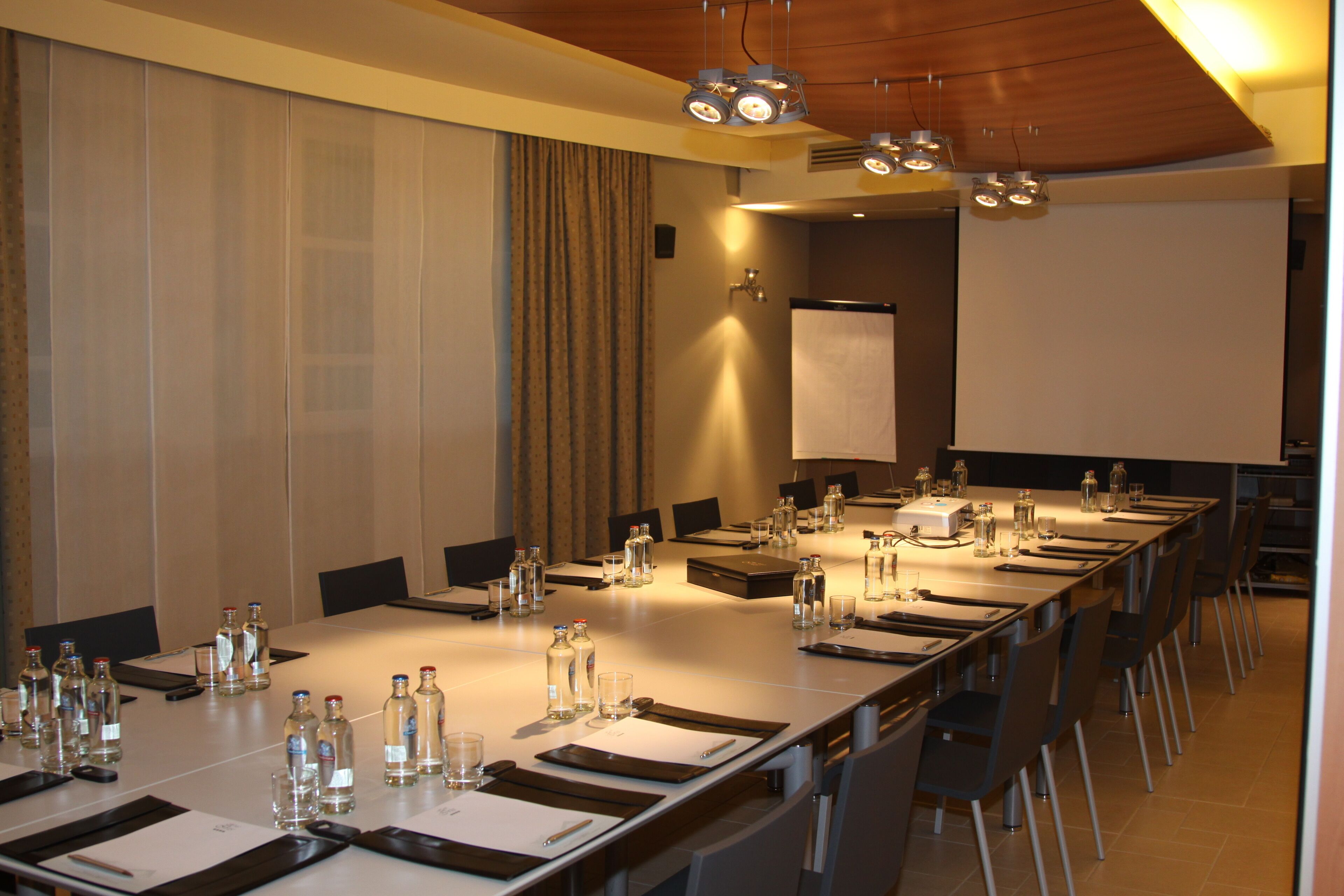 Un salón de conferencias con una mesa larga, sillas y una pantalla para proyector.