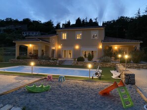 Ein zweistöckiges Haus mit Swimmingpool, Sitzgelegenheiten im Freien und einem gut beleuchteten Patio.