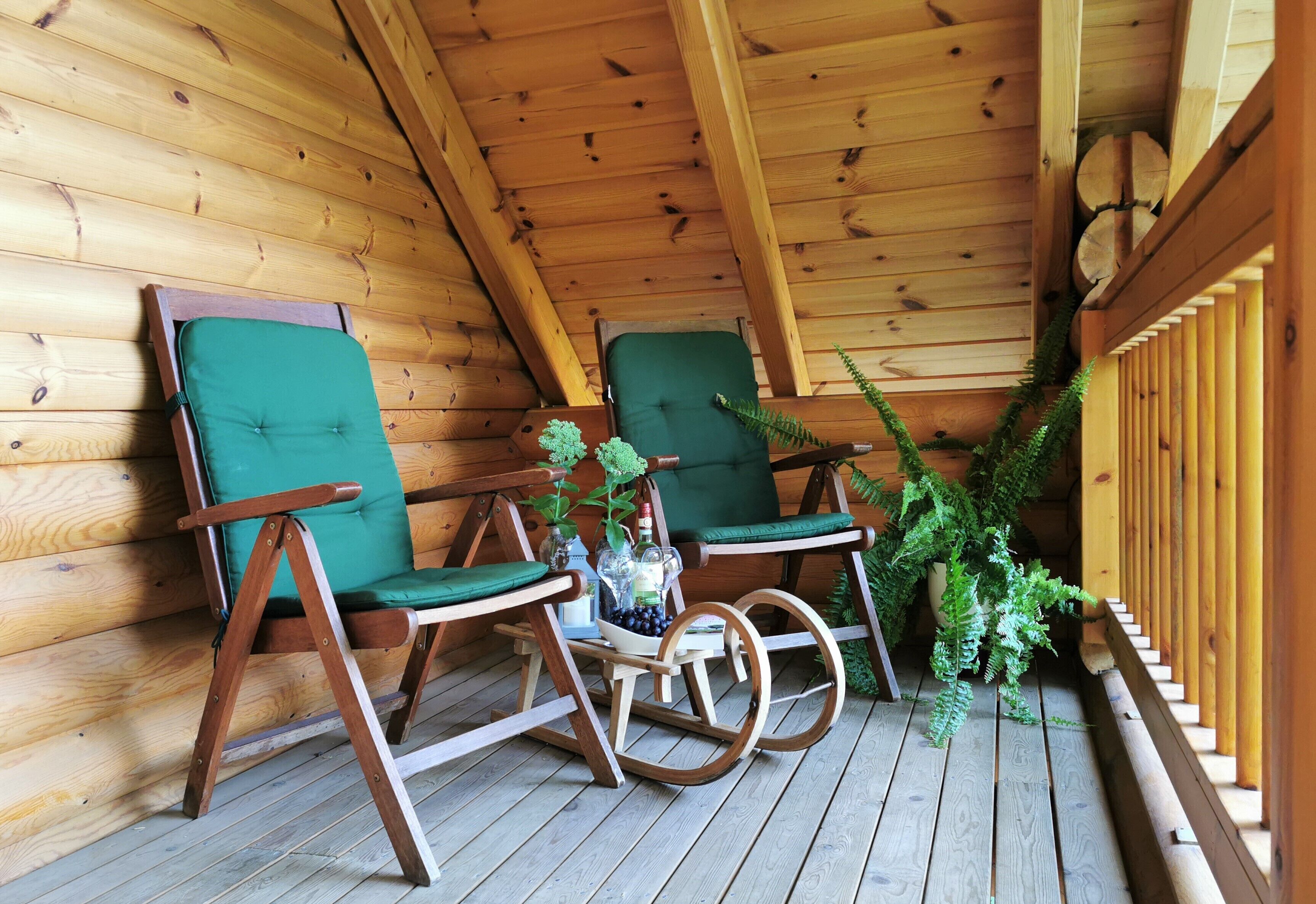 Une terrasse en bois avec deux fauteuils à bascule et une petite table sur laquelle est posé un vase de fleurs.