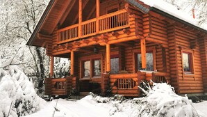 Una cabaña de troncos con balcón y porche, rodeada de árboles cubiertos de nieve.