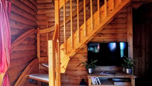 Una escalera de madera que lleva a una sala de estar con un televisor de pantalla plana, armarios de madera y plantas en macetas.