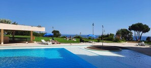 A pool area with lounge chairs and umbrellas, a covered seating area, and a view of the sea. - Cascais by the Sea (Cascais)