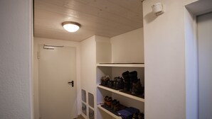 Pasillo con una puerta blanca, una lámpara en el techo y estantes con zapatos.