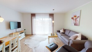Una sala de estar moderna con sofá, televisor, mesa de comedor y un ventanal grande.