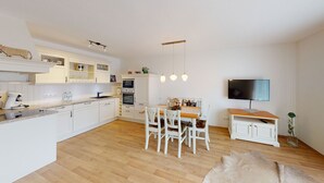 Una cocina moderna con armarios blancos, un comedor con mesa y sillas de madera y un televisor de pantalla plana montado en la pared.