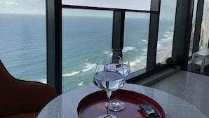 Una mesa con un vaso de agua y una bandeja, con vista a una playa y al océano desde un edificio de gran altura.