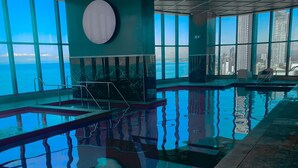 Una piscina interior con agua azul cristalina, grandes ventanales que dan al mar y un diseño de techo moderno.