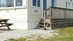 Una casa móvil con un cartel con el número 99, una terraza de madera y una mesa de picnic.