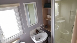 Un baño pequeño con inodoro, lavamanos y ducha. Hay ventanas y un espejo en la pared.