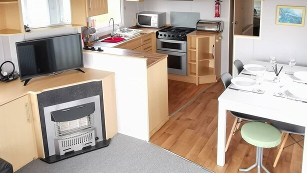 Cocina compacta con armarios de madera, microondas, estufa y un pequeño comedor con mesa y sillas.