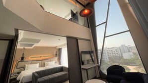 A modern hotel room with a large bed, a sofa, a small table, and a TV. There is a large window providing a view of the city. - Amethyst Hotel Pattaya (Pattaya)
