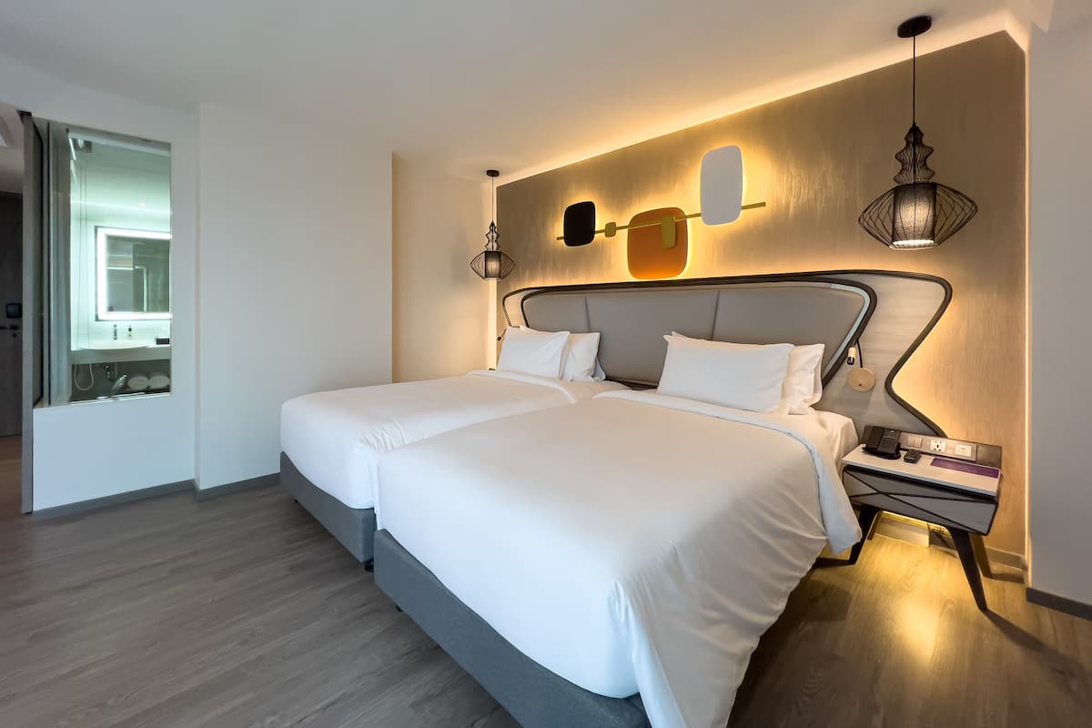 Moderni hotellihuone, jossa on suuri sänky, yöpöydät, peili ja seinään kiinnitetty valaisin.