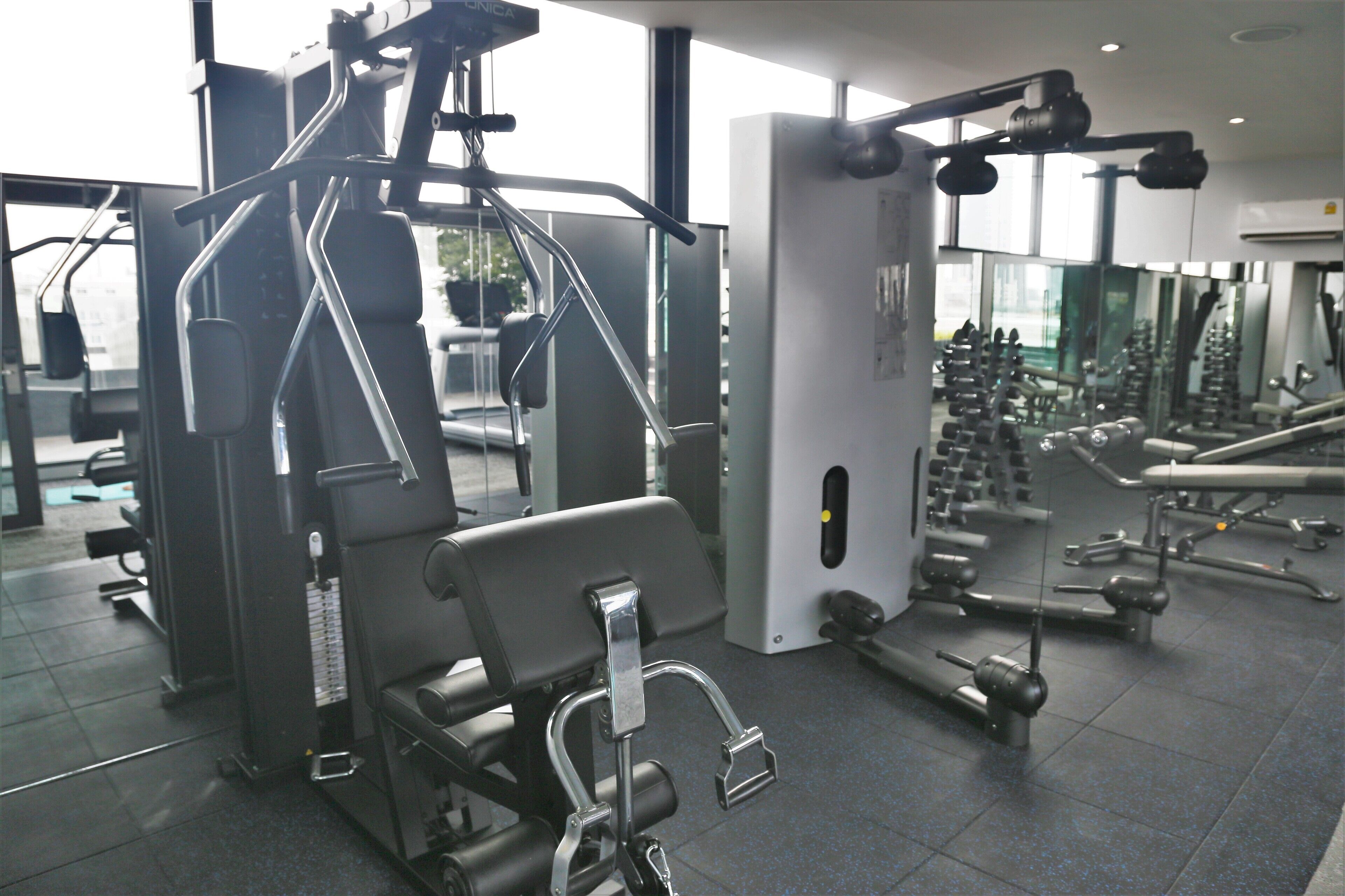 A gym with various exercise machines, a mirrored wall, and a tiled floor.