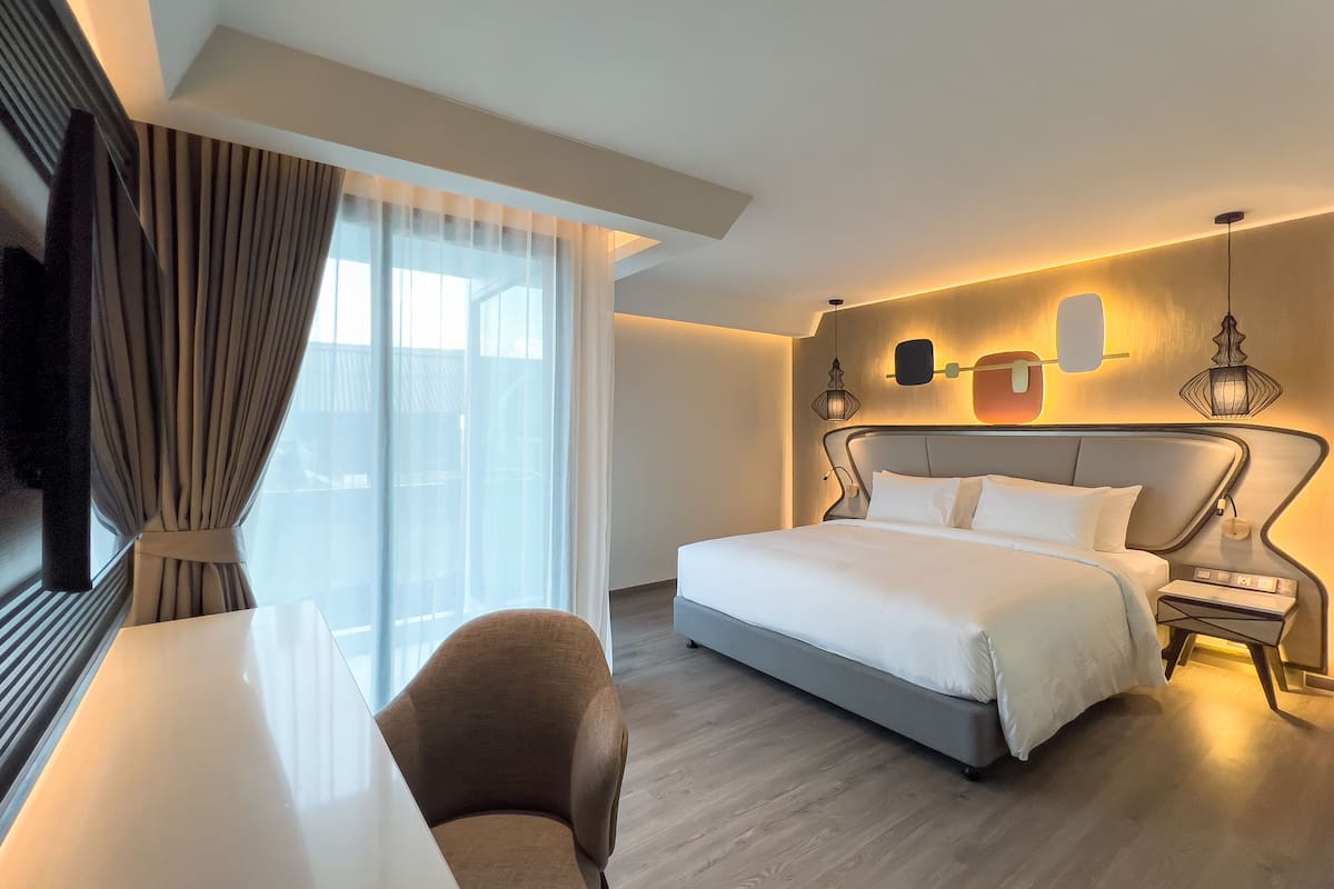 Moderni hotellihuone, jossa on sänky, yöpöytä, tuoli ja suuri ikkuna, jossa on verhot.