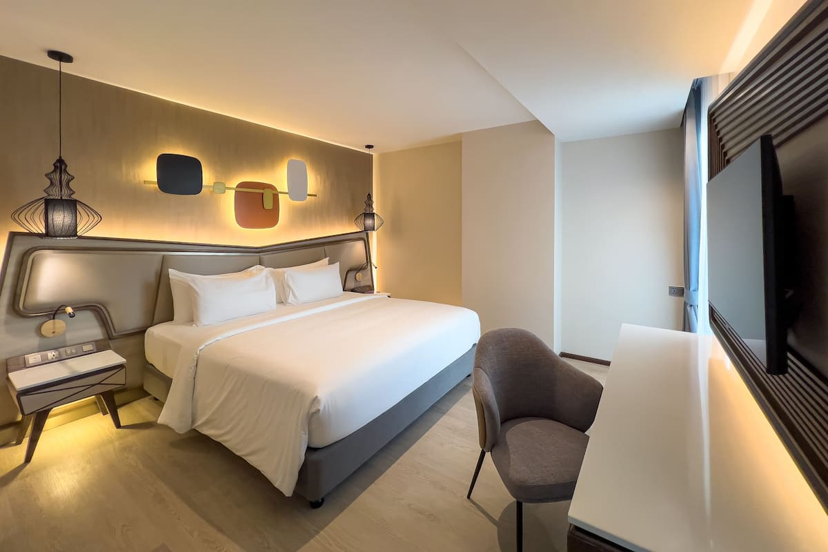 Moderni hotellihuone, jossa on suuri sänky, yöpöytä, lamppu ja seinälle asennettu televisio.