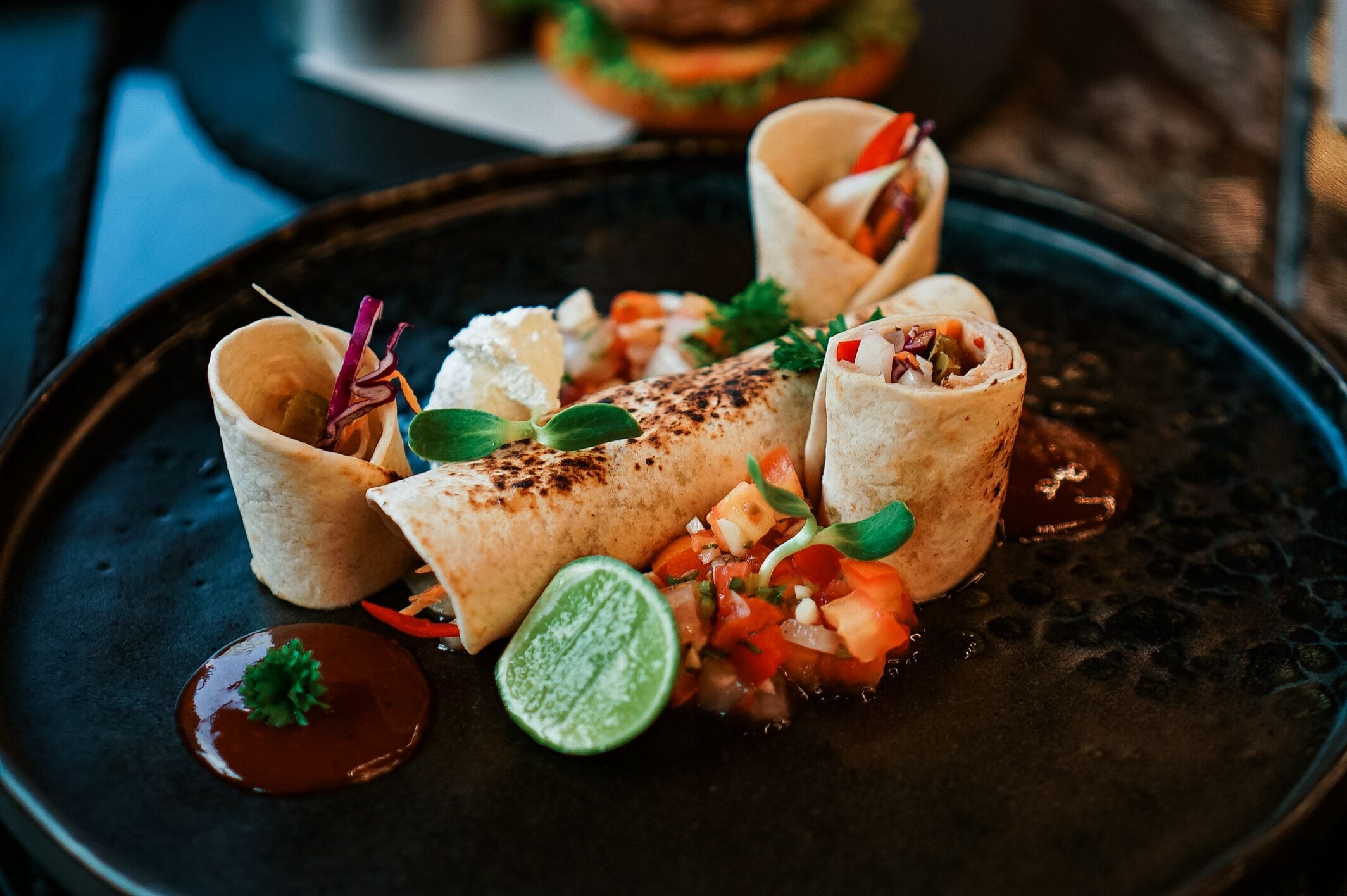 Un plato con tres wraps, una cuña de lima y salsa.