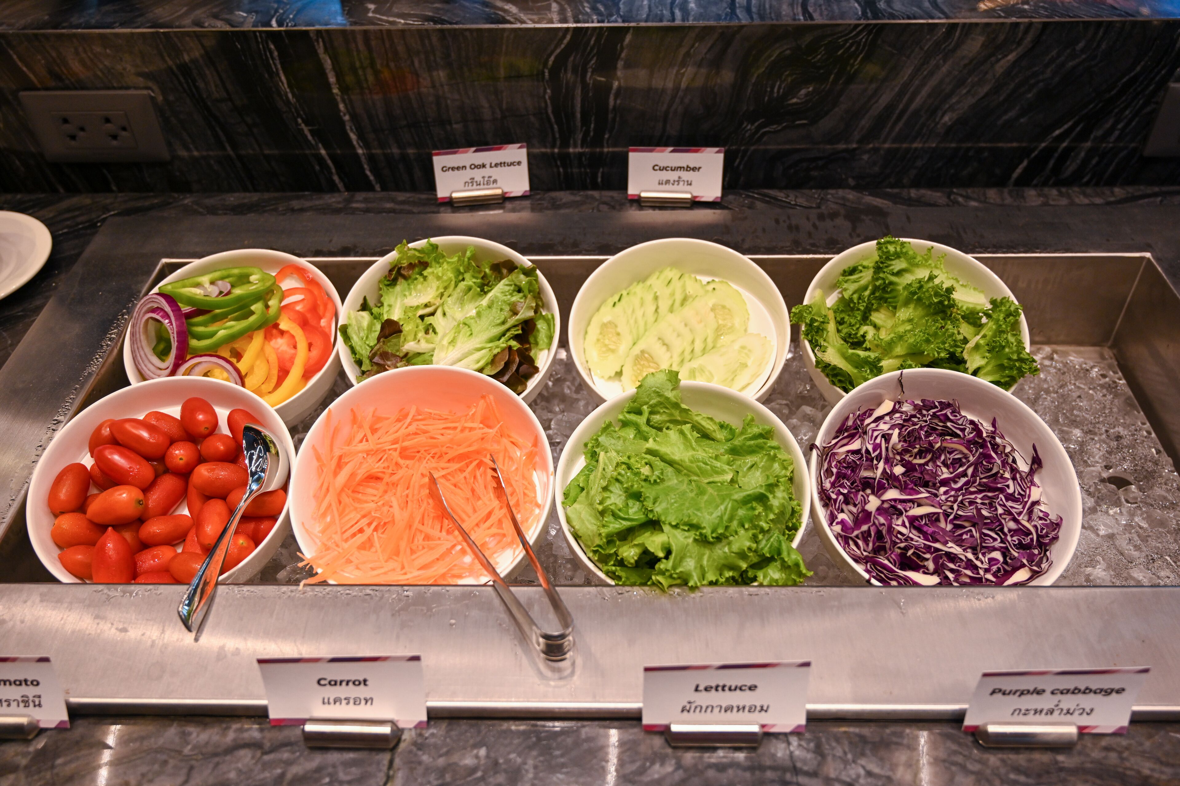 A salad bar with various vegetables like tomatoes, carrots, lettuce, and purple cabbage.