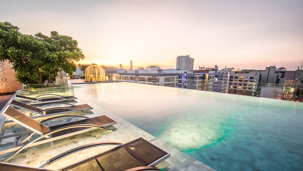 A rooftop infinity pool with sun loungers and a view of the city skyline at sunset. - Amethyst Hotel Pattaya (Pattaya)