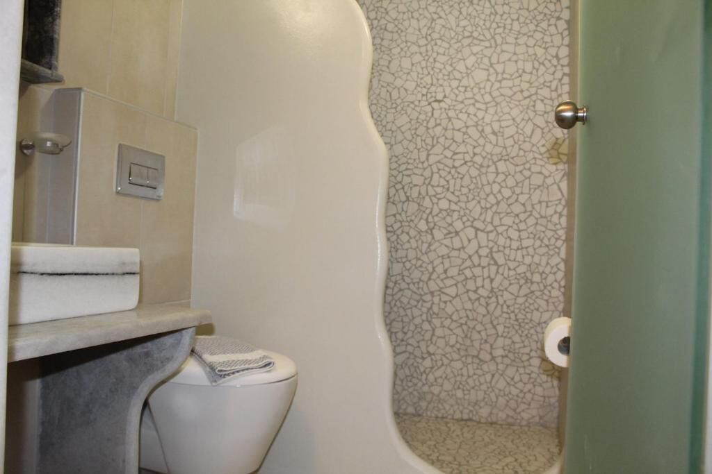 Une salle de bain avec des toilettes, un porte-serviettes et une douche dont le mur est recouvert de carreaux fissurés.
