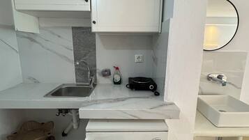 Una cocina compacta con armarios blancos, un lavamanos empotrado, un refrigerador pequeño y una encimera con una tetera y una cafetera.