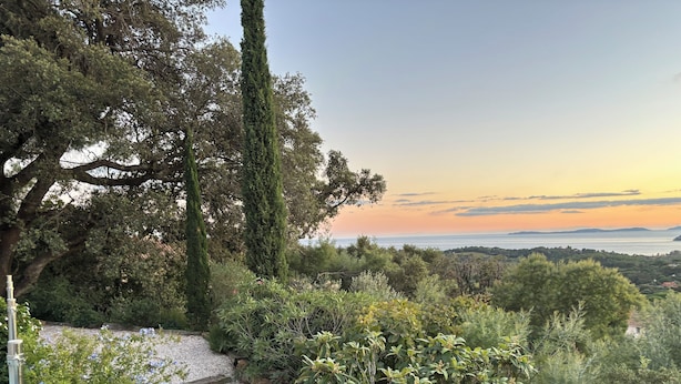 A garden with a stone pathway, various plants, and a view of the sea at sunset. - 1st level villa overlooking the sea and the village - 300m from shops and restaurants (La Croix-Valmer)