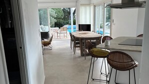 A modern kitchen with a dining area, large windows, and a view of a swimming pool. - 1st level villa overlooking the sea and the village - 300m from shops and restaurants (La Croix-Valmer)