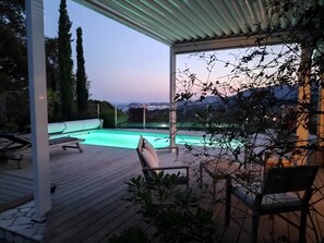 Ein Poolbereich mit Liegestühlen und Blick auf das Meer im Abendlicht.