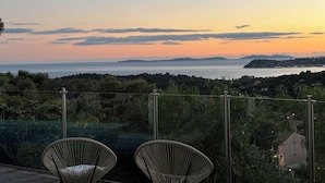 A terrace with wicker chairs overlooking a coastal landscape during sunset. - 1st level villa overlooking the sea and the village - 300m from shops and restaurants (La Croix-Valmer)