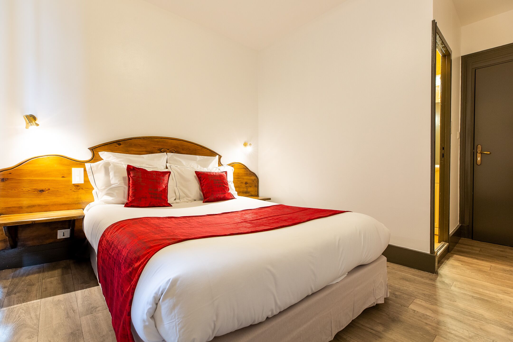 A neatly made bed with white and red bedding, a wooden headboard, and bedside lamps.