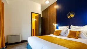 A hotel room with a large bed, a wooden headboard, a wall-mounted artwork, and a window with curtains. - Grand Hôtel 1899 (Langogne)