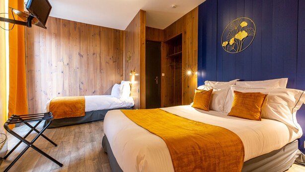 A hotel room with two beds, wooden paneling, a flat-screen TV, and a decorative wall piece. - Grand Hôtel 1899 (Langogne)