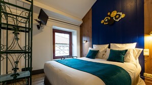 A bedroom with a bed, a window, a wall-mounted TV, and a decorative wall piece. - Grand Hôtel 1899 (Langogne)
