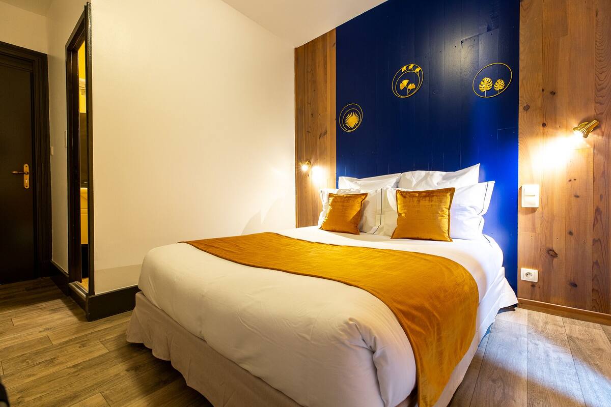 A hotel room with a bed, wooden panel wall, and decorative wall lights.