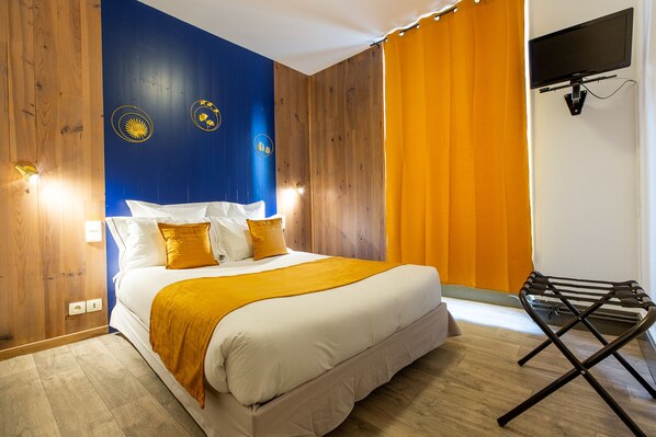 A neatly made bed with white linens and a yellow throw, a wooden wall with a blue section, and a black folding chair. - Grand Hôtel 1899 (Langogne)
