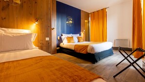 A hotel room with a wooden accent wall, a bed with white and gold bedding, a blue accent wall, and a standing heater. - Grand Hôtel 1899 (Langogne)